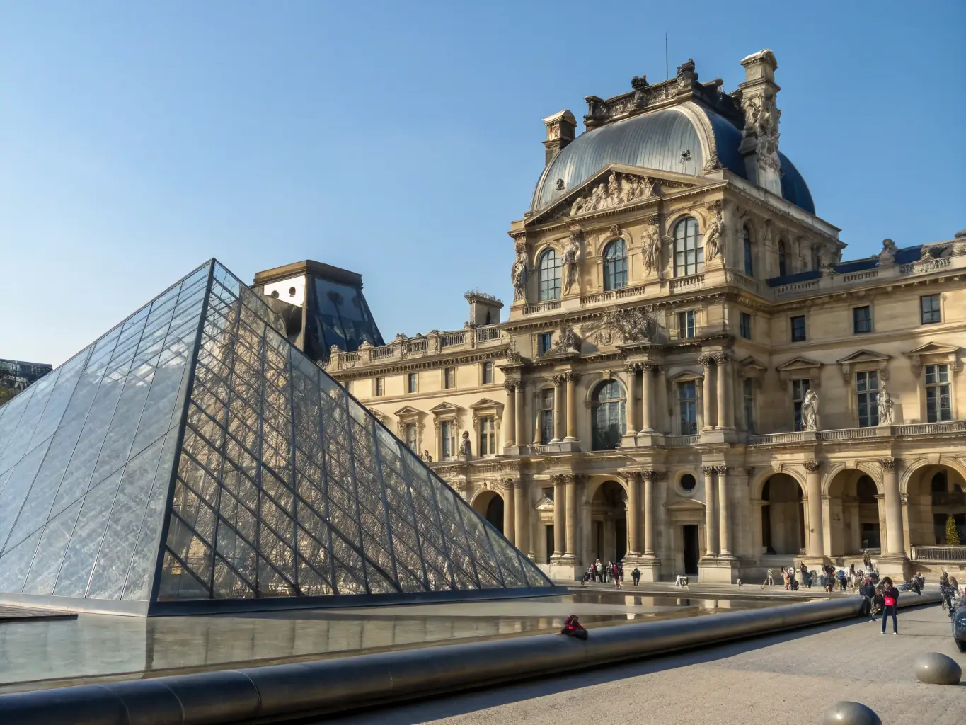 A grand and classic view of the Louvre Museum, with the iconic glass pyramid in the foreground and the historic palace in the background, symbolizing centuries of art and history.